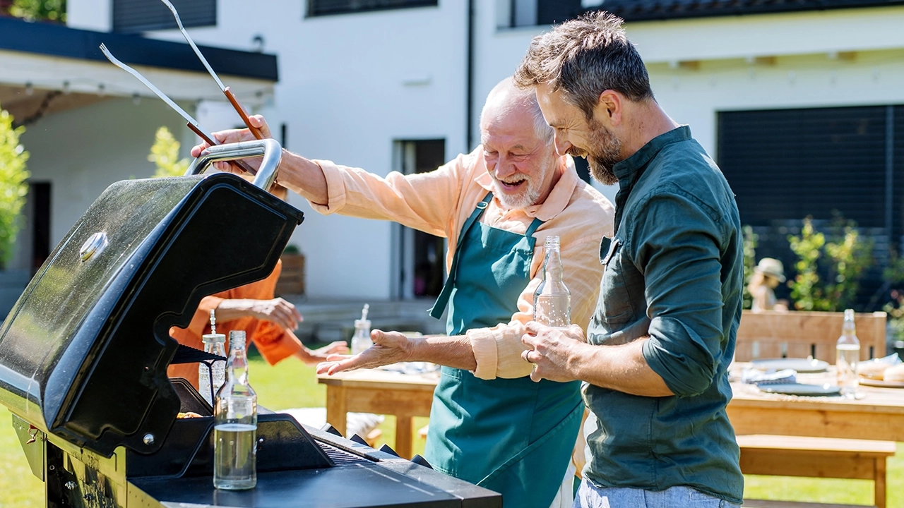 Maenner stehen gemeinsam im Garten am Grill preview