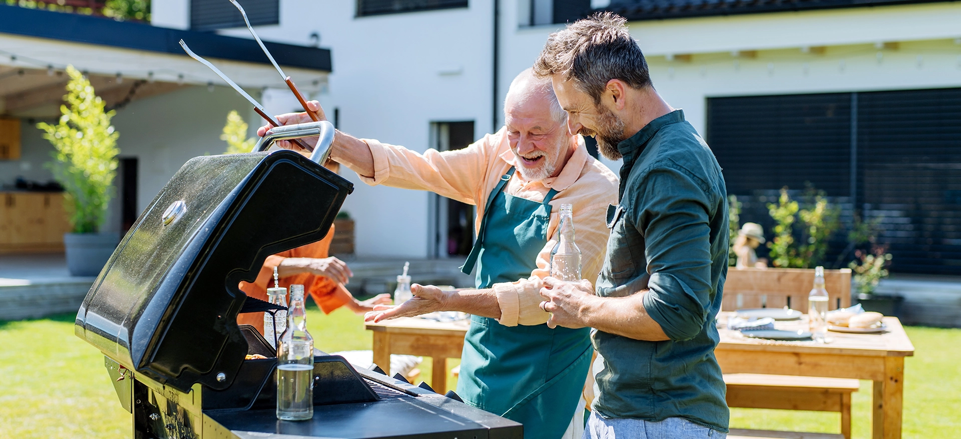 Maenner stehen gemeinsam im Garten am Grill